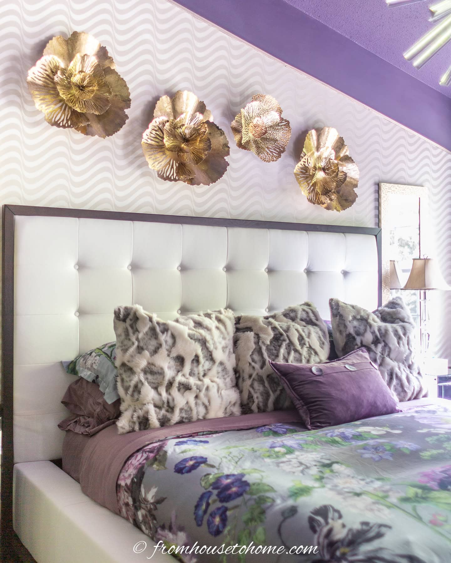 4 gold flower wall sculptures hung above a white bed in a purple bedroom