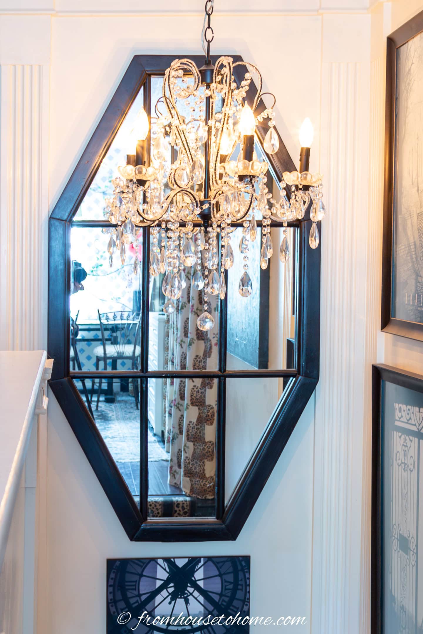 a mirror window hung at the top of the stairwell with a chandelier in front