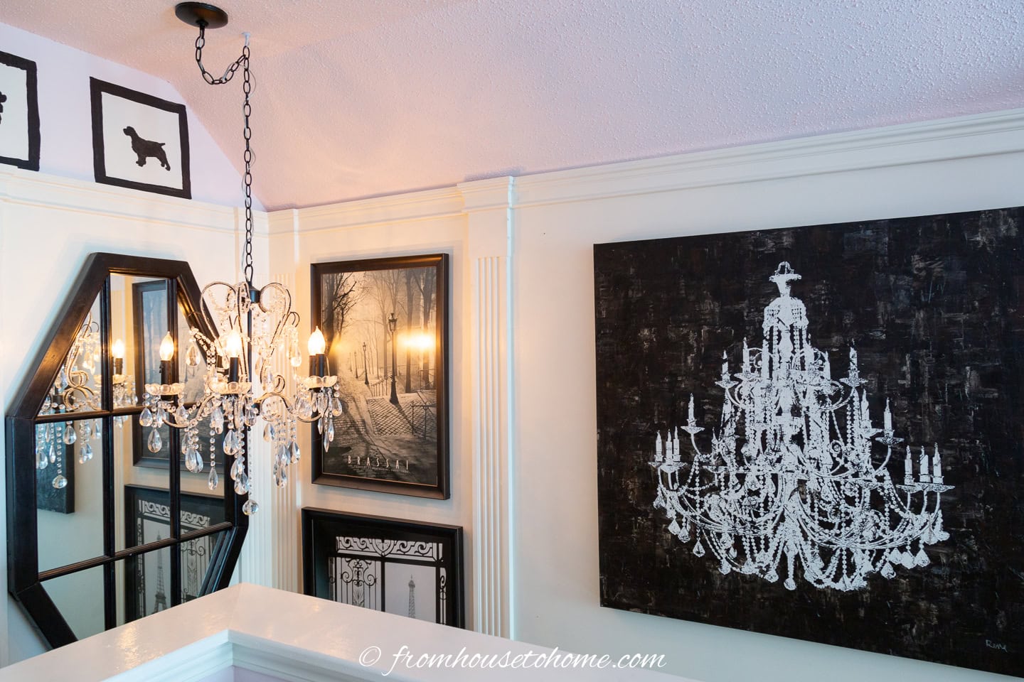 a stairwell gallery wall with black and white pictures, a mirror window and a chandelier