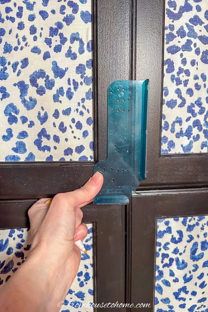 A template being used to mark knob locations on kitchen cabinet doors