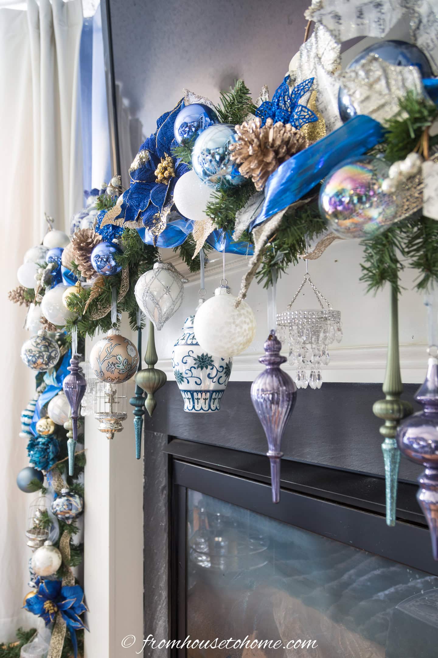Blue and white Christmas ornaments hanging from a garland in front of a fireplace
