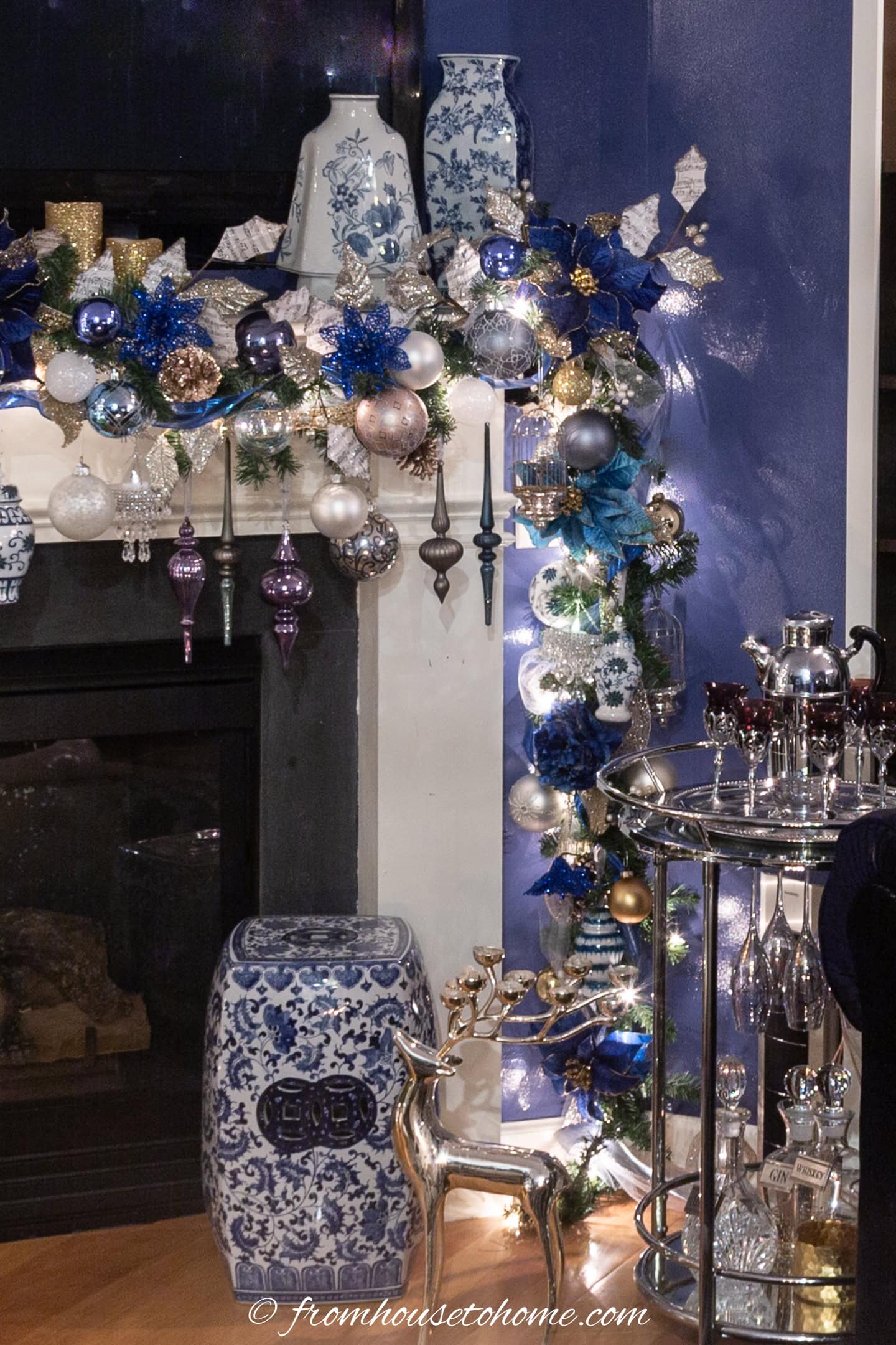 A blue and white garden stool in front of a fireplace decorated with a blue and white Christmas garland and ginger jars