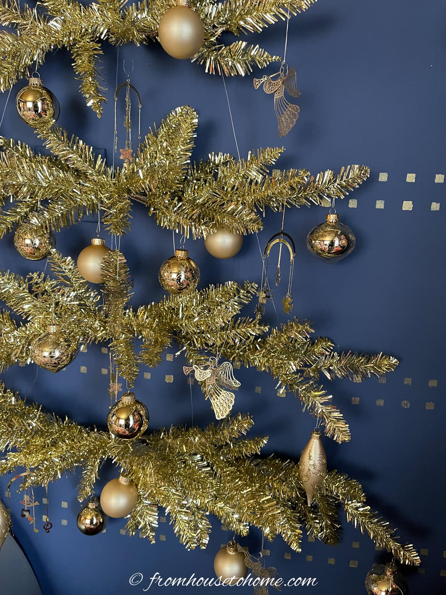 A few gold ornaments hanging from a wall Christmas tree