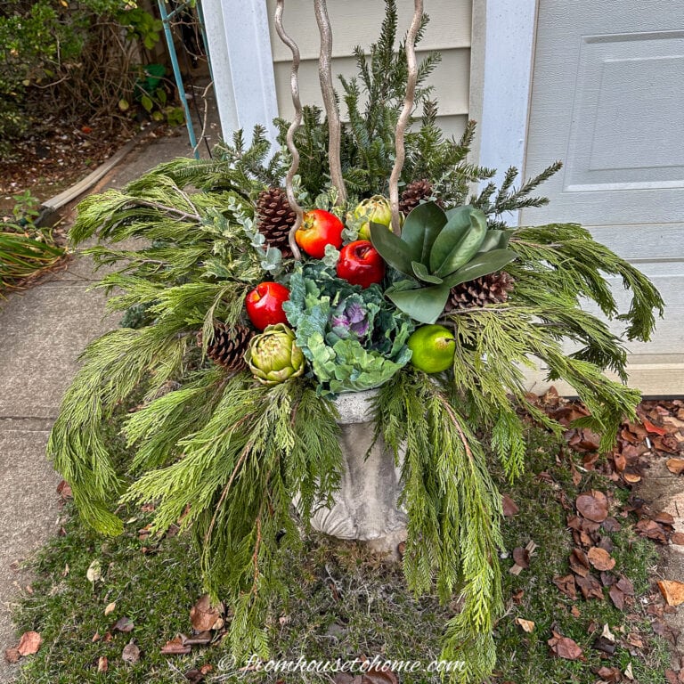 diy winter porch pot with cedar boughs, fir branches, magnolia leaves, holly branches, artificial fruit, ornamental cabbage, and gold manzanita branches