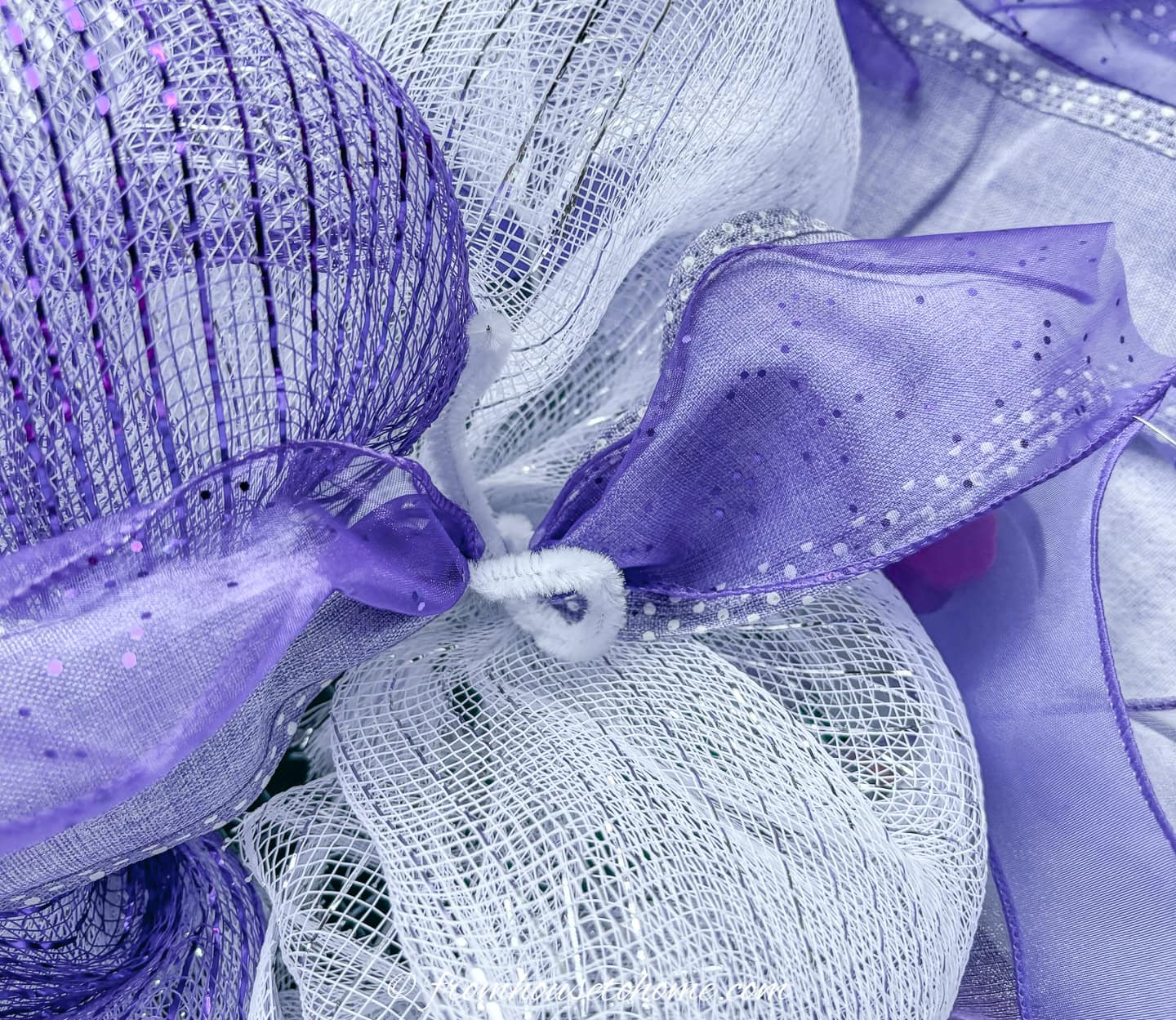 ribbon being attached to a deco mesh Christmas wreath with pipe cleaners