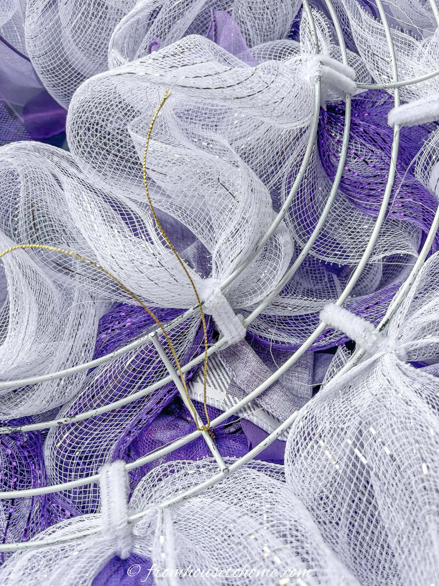 A bow being attached to a purple and white deco mesh pouf Christmas wreath with florist wire