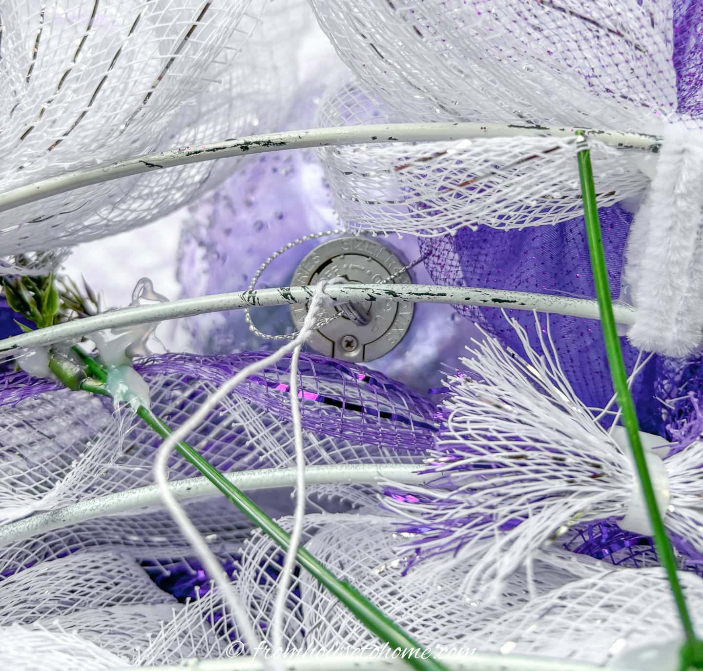 purple Christmas ball ornament being attached to a lavender and white deco mesh pouf Christmas wreath with florist wire