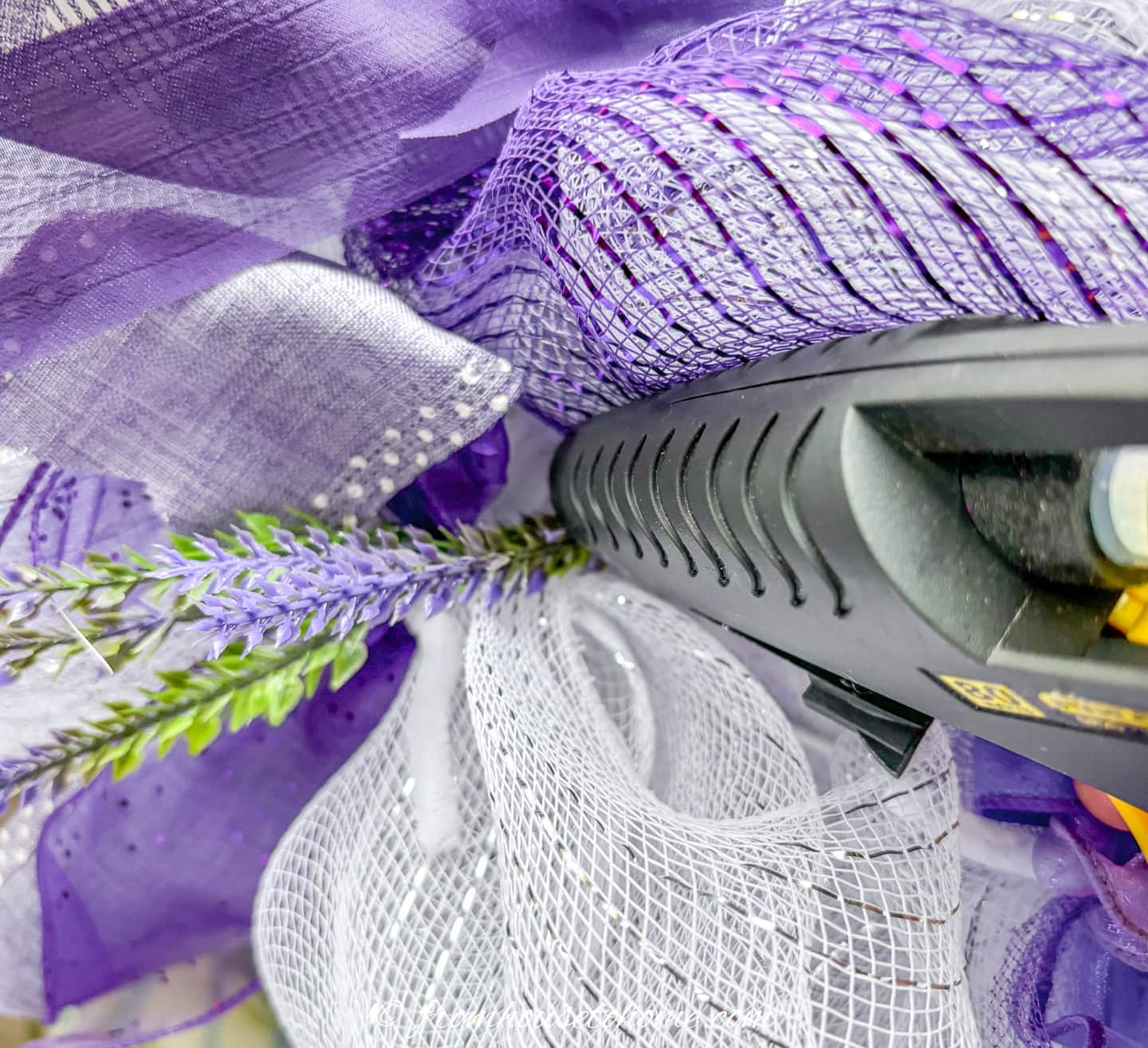 artificial lavender picks being hot glued onto a purple and white deco mesch pouf Christmas wreath