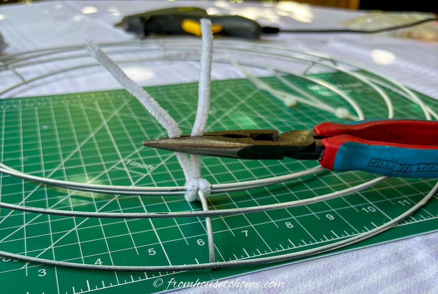 ends of a pipe cleaner being twisted onto a wire wreath form with a needle nose pliers