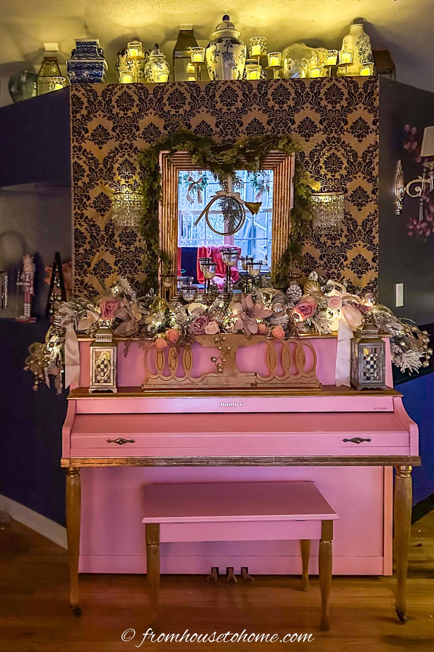 A shelf full of flameless candles and ginger jars above a pink piano decorated for Christmas