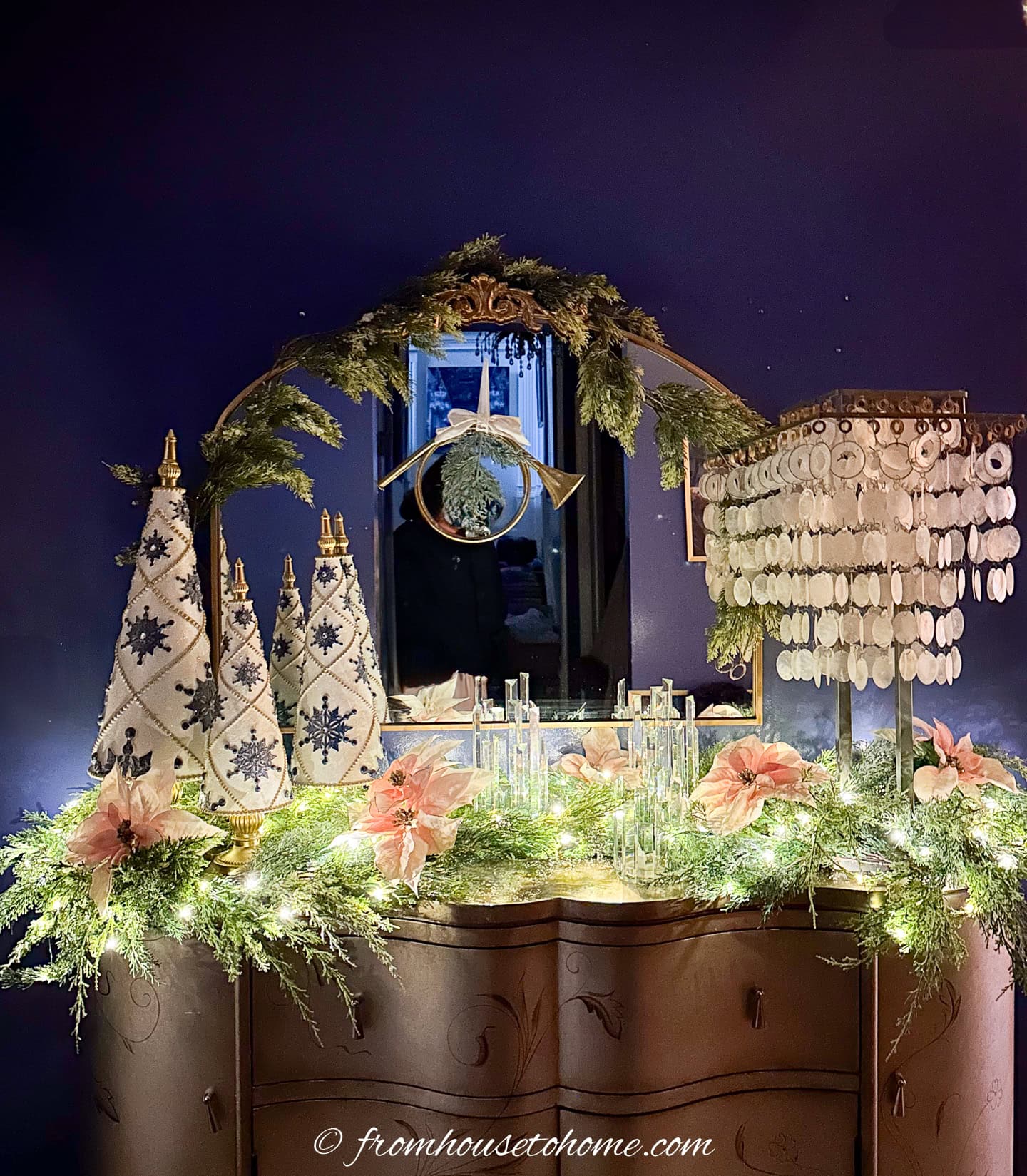 An evergreen garland with pink poinsettias and lights on a front hall console table with a mirror above it