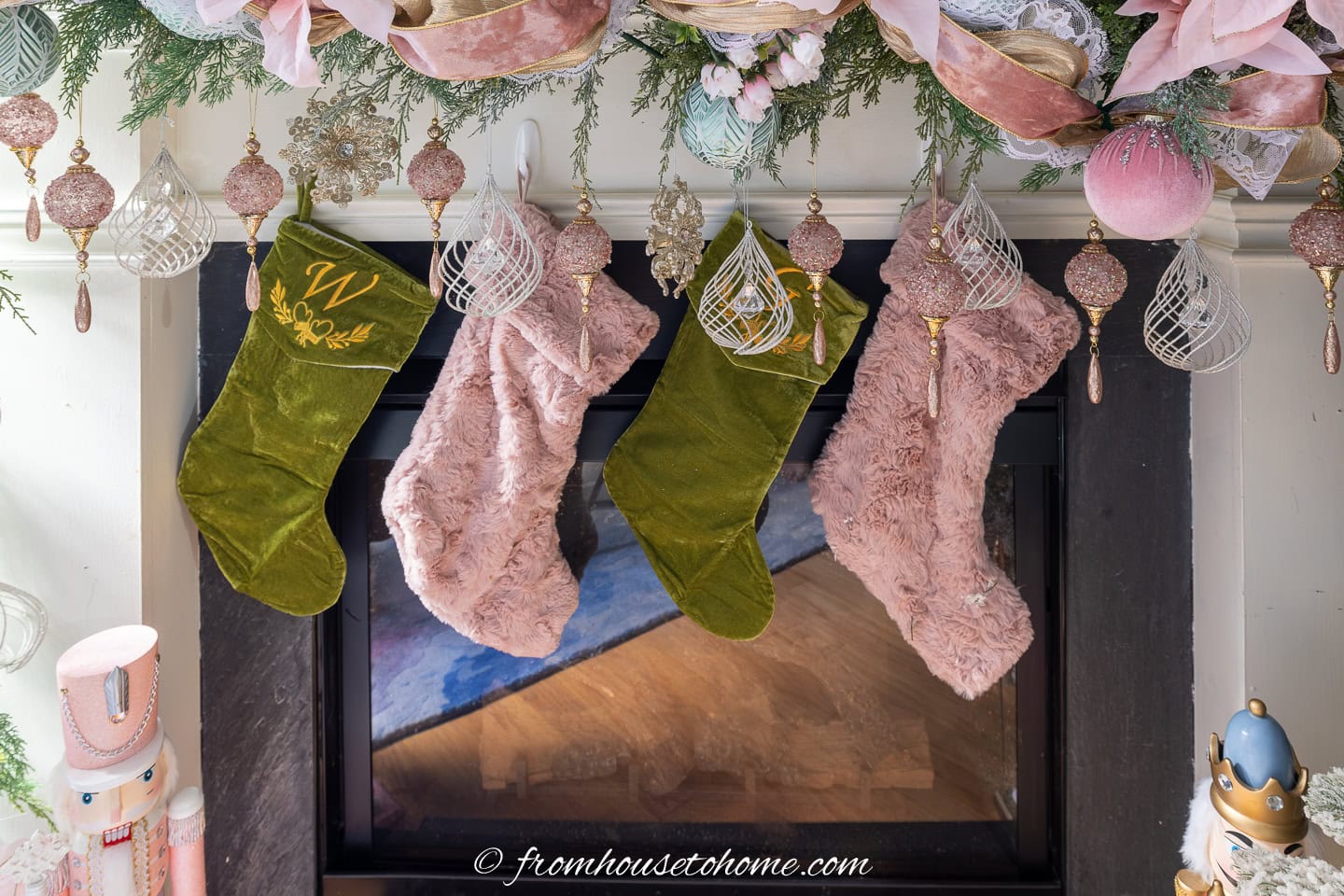 pink and green stockings hung on a fireplace under a pink and gold garland