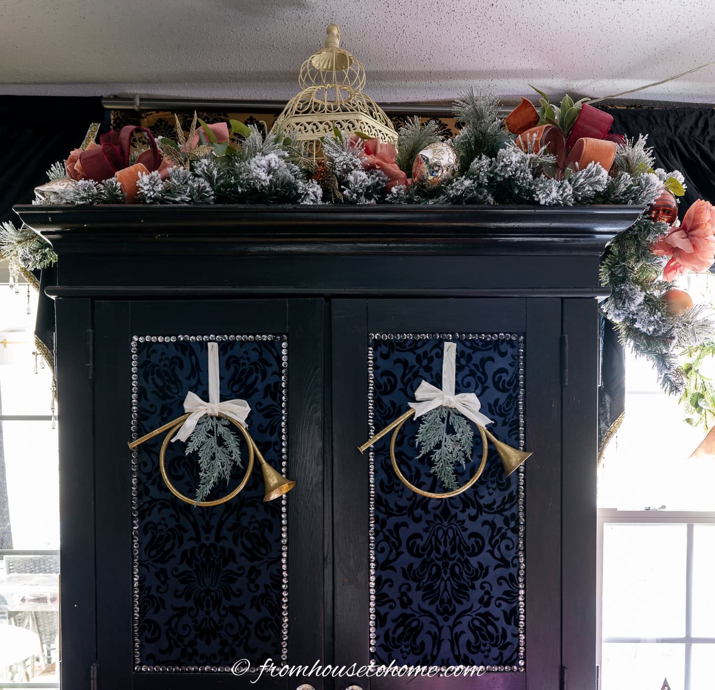 An armoire with a pink garland on the top of it and horn ornaments hung on the doors