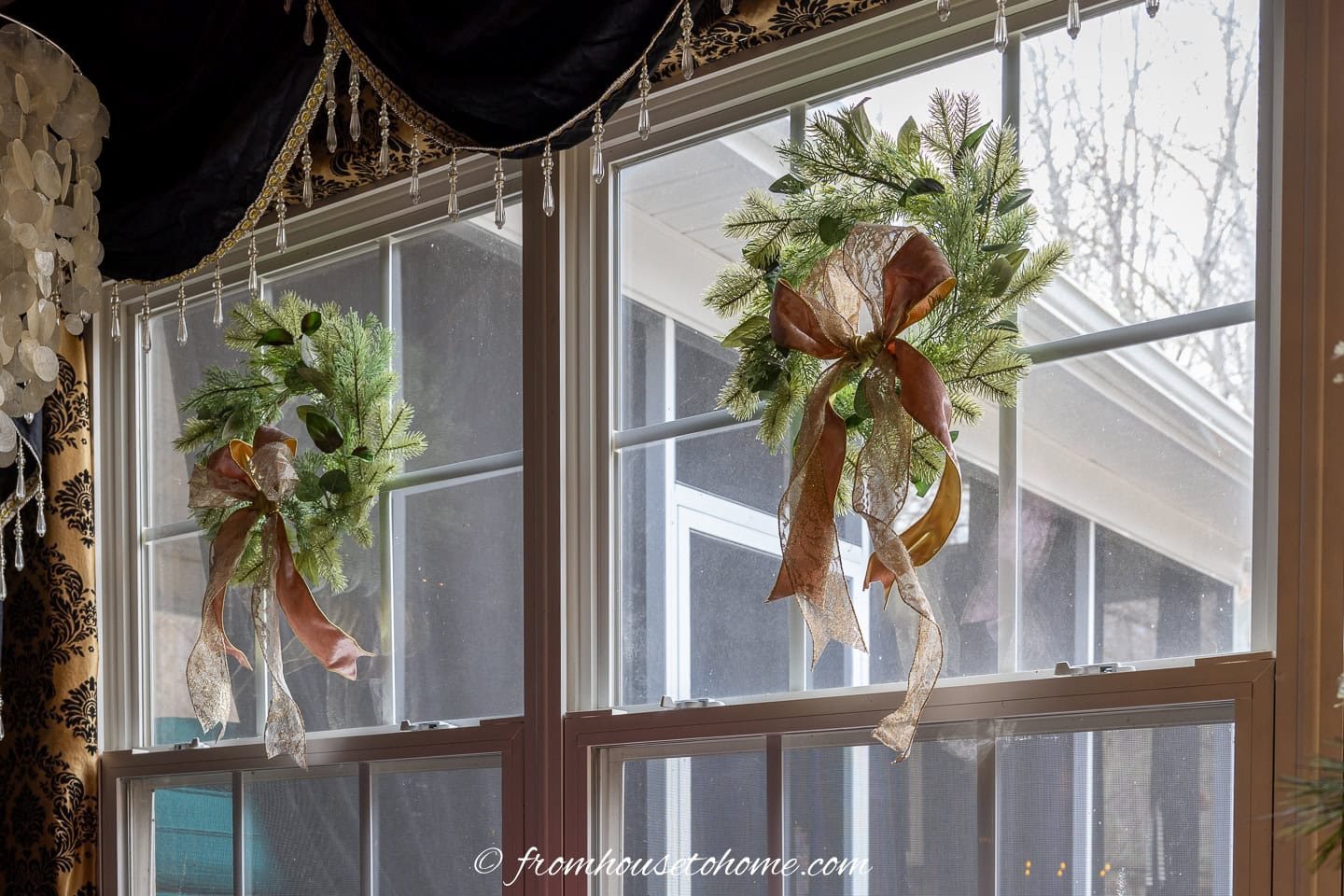 Evergreen wreaths with pink and gold bows hung on a large window
