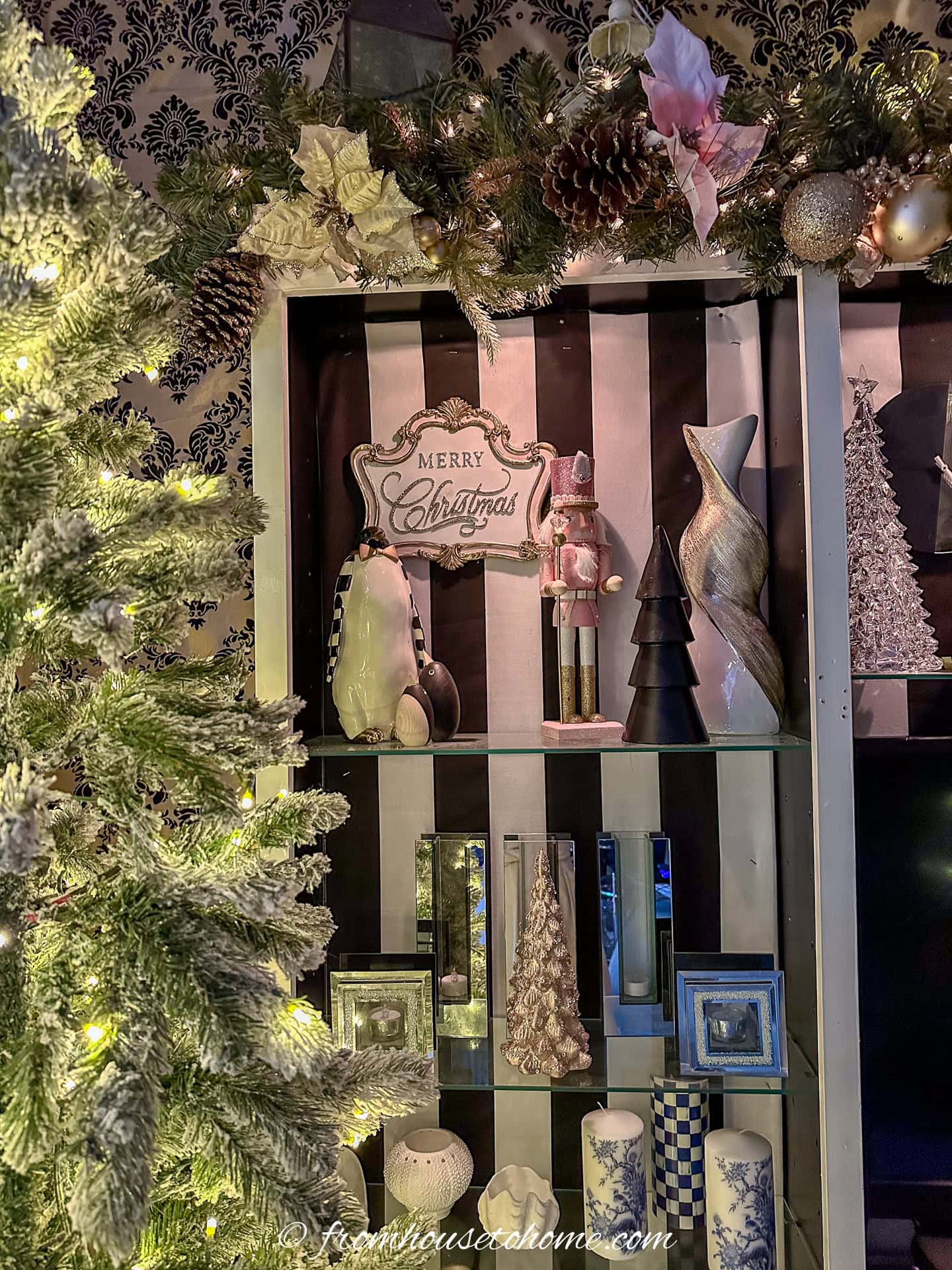 A bookshelf decorated for Christmas with a pink nutcracker and mini Christmas trees
