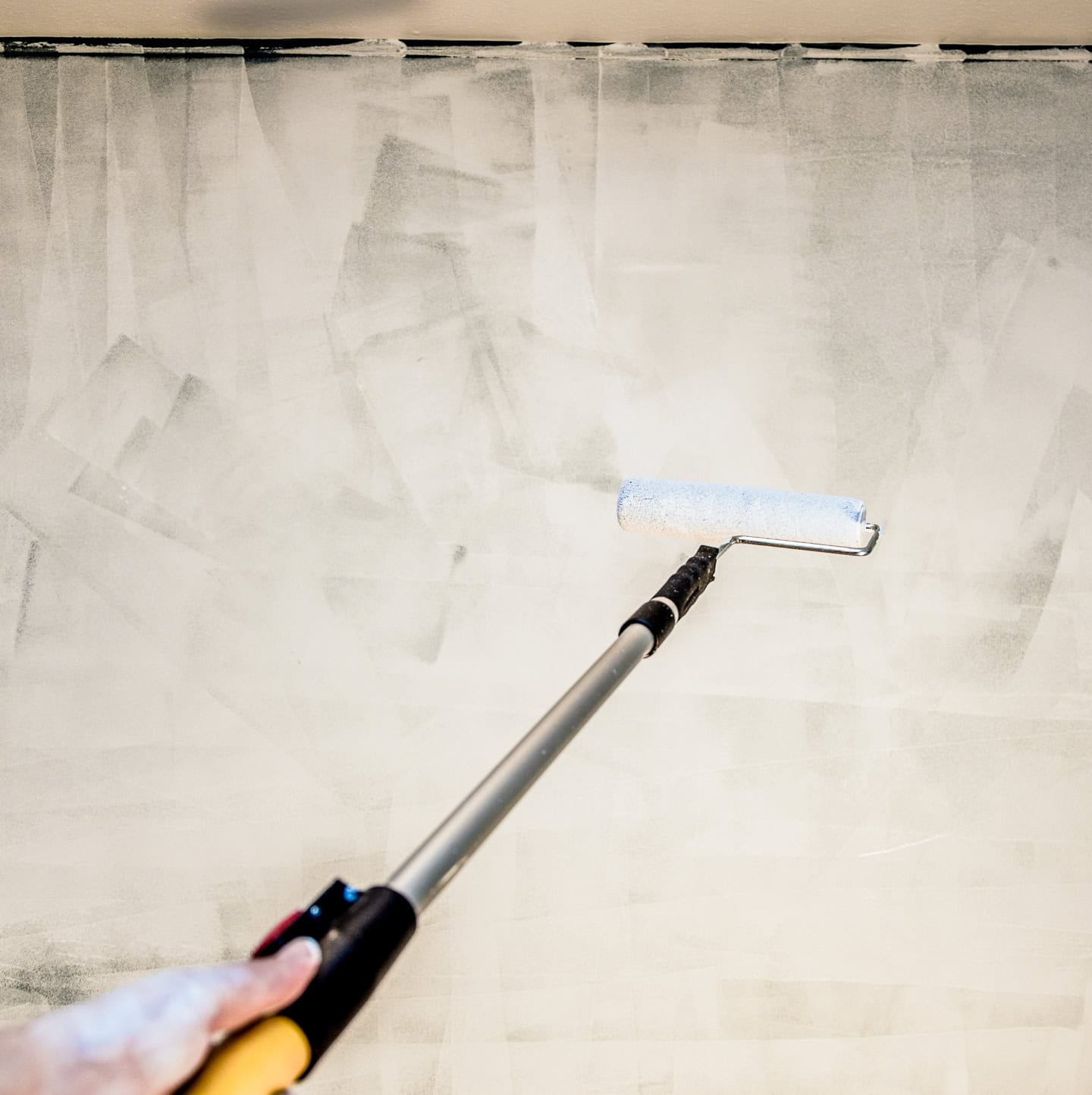a paint roller on an extension priming the ceiling