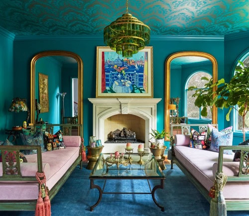 A glam living room with teal walls, pink sofas, gold mirrors and a teal and gold wallpaper on the ceiling