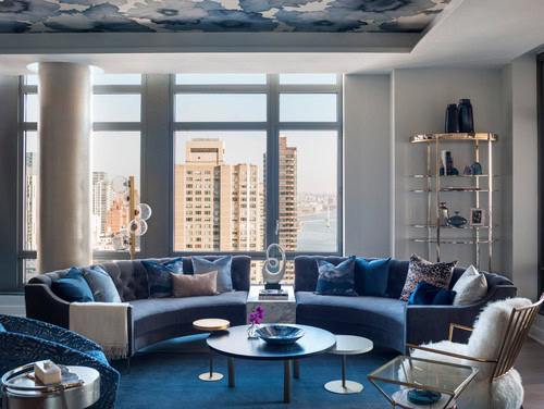 A living room with a blue circular sofa and blue and white floral wallpaper on the ceiling