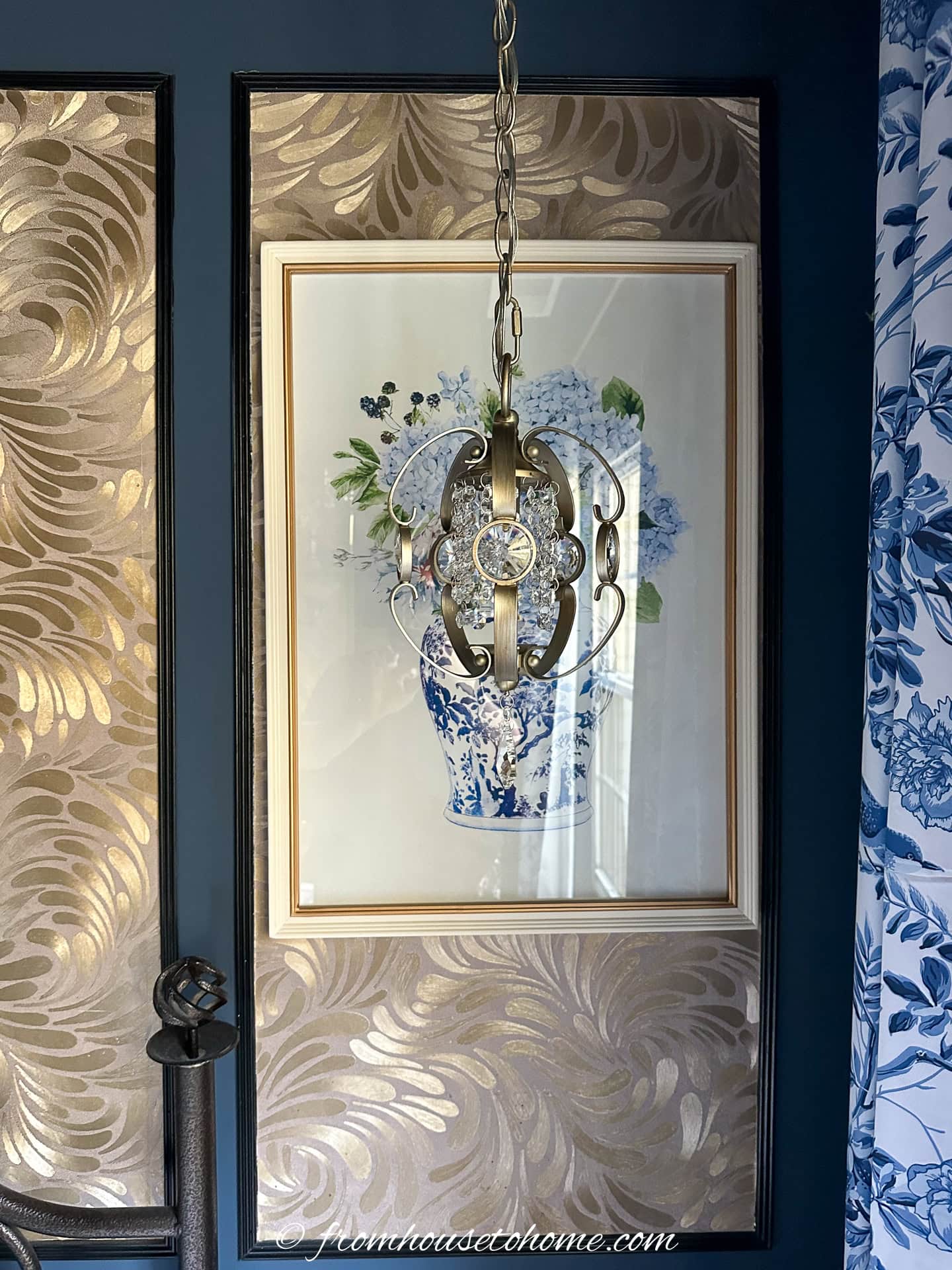A gold light fixture hung in front of a picture and panels covered with gold wallpaper