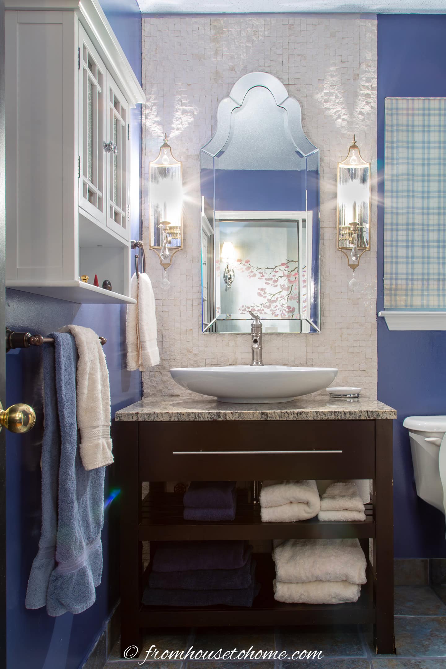 A guest bathroom with a split-face lime stone backsplash behind the vanity, a tall Venetian mirror and Art Deco style sconces