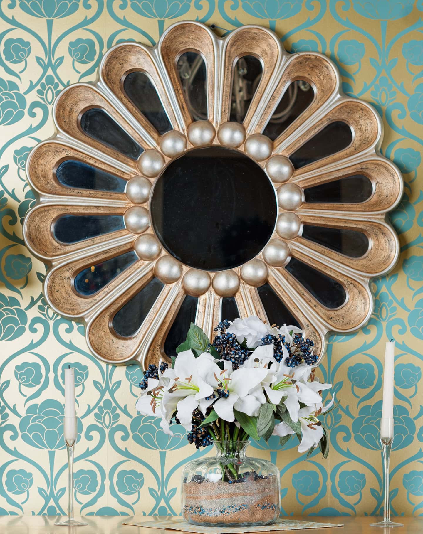 A starburst mirror hung on a gold and blue wallpapered wall