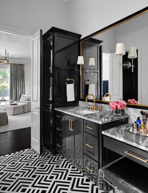 An Art Deco bathroom with black lacquer cabinets, black and white marble countertops, gold faucets and a geometric tile floor