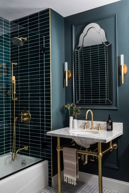 A green Art Deco bathroom with a large Venetian mirror over a white sink with gold faucets