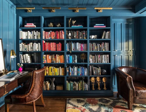 A blue library wall with gold picture lights above it
