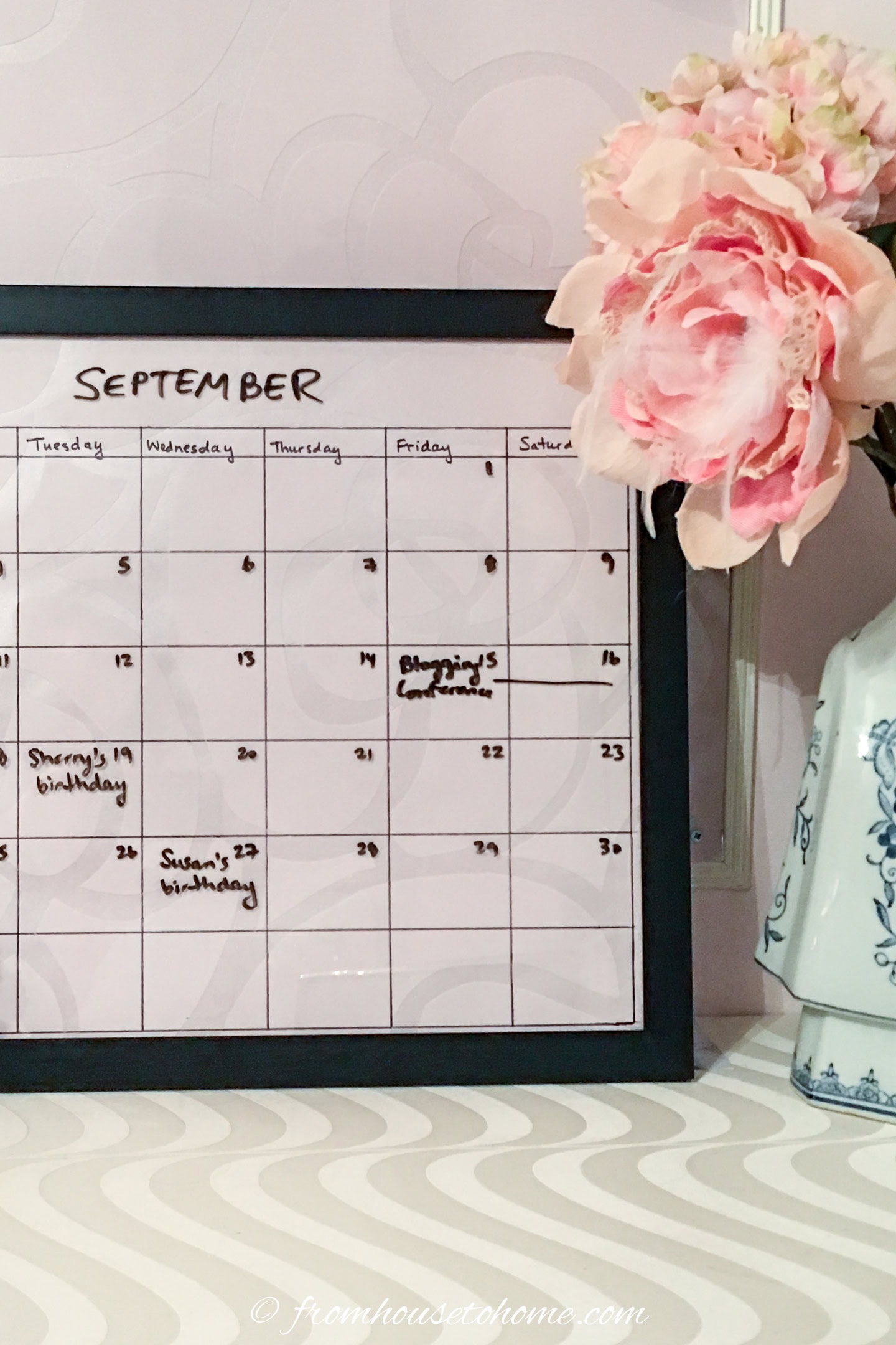 A pink DIY dry erase calendar made with wallpaper and a black frame