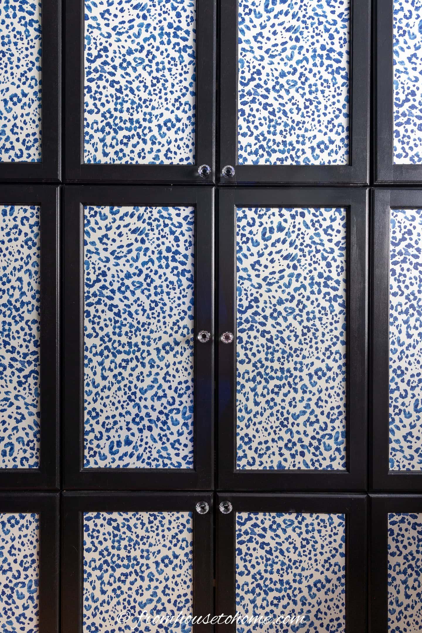 A set of black-framed cabinet doors with panels featuring wallpaper with a white background and blue leopard print pattern.