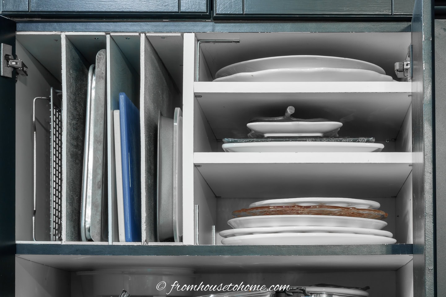 A kitchen cabinet with vertically organized baking sheets and cutting boards on the left, and neatly stacked serving trays and platters on the right.