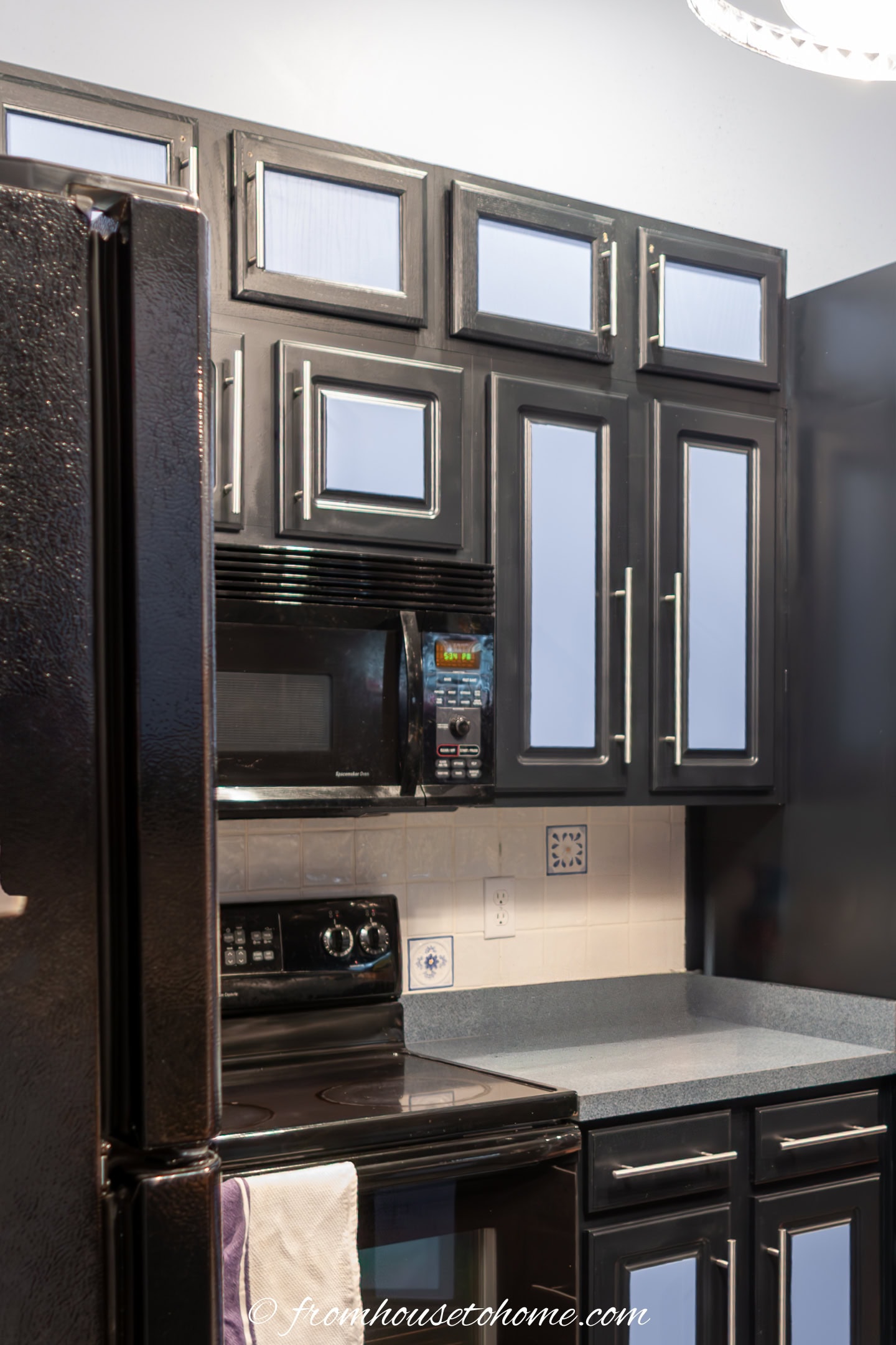 A modern kitchen with black cabinets featuring light blue panels, stainless steel handles, a black oven, black microwave, and gray countertops.