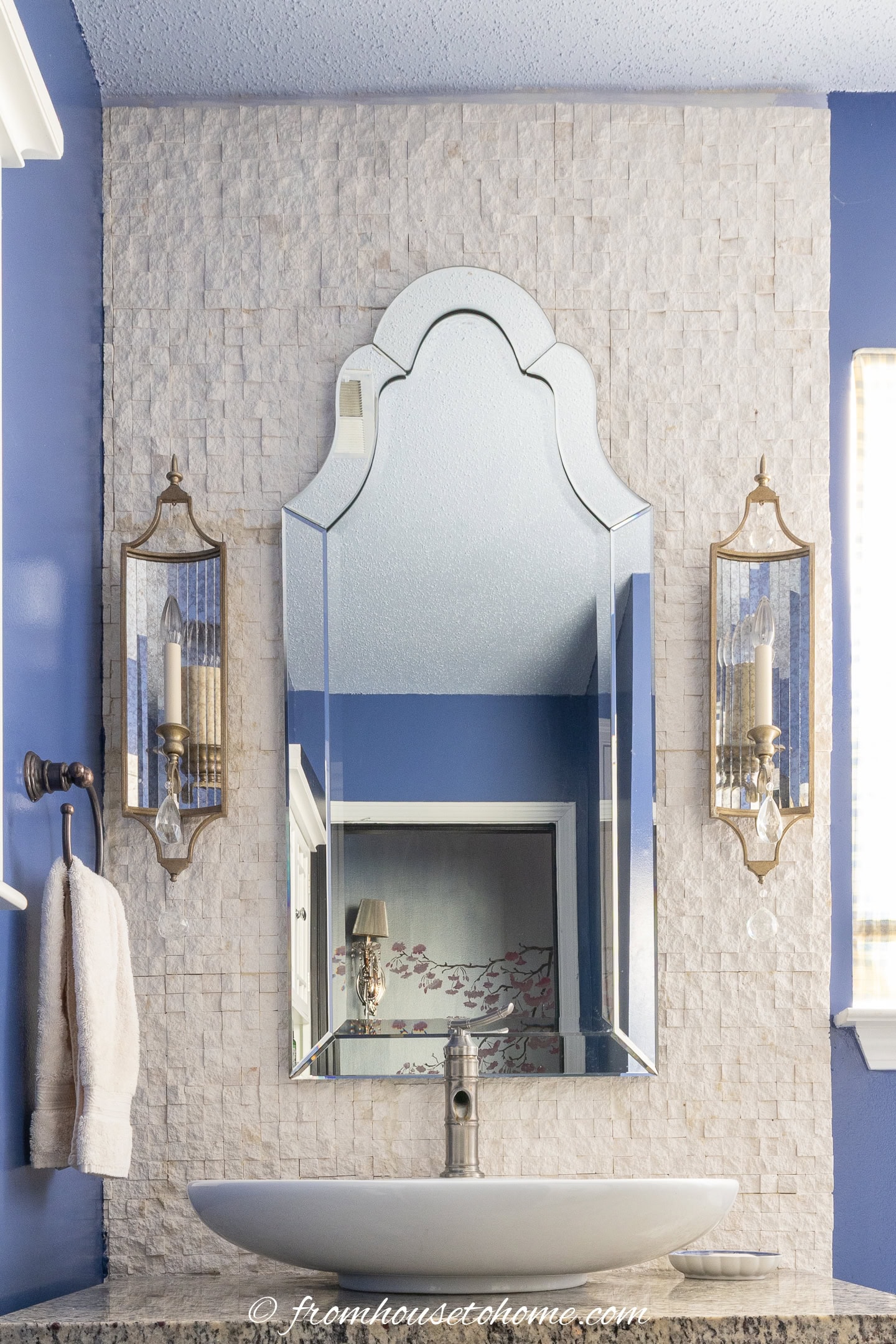 A splitface limestone wall behind a bathroom vanity, venetian mirror and wall sconces