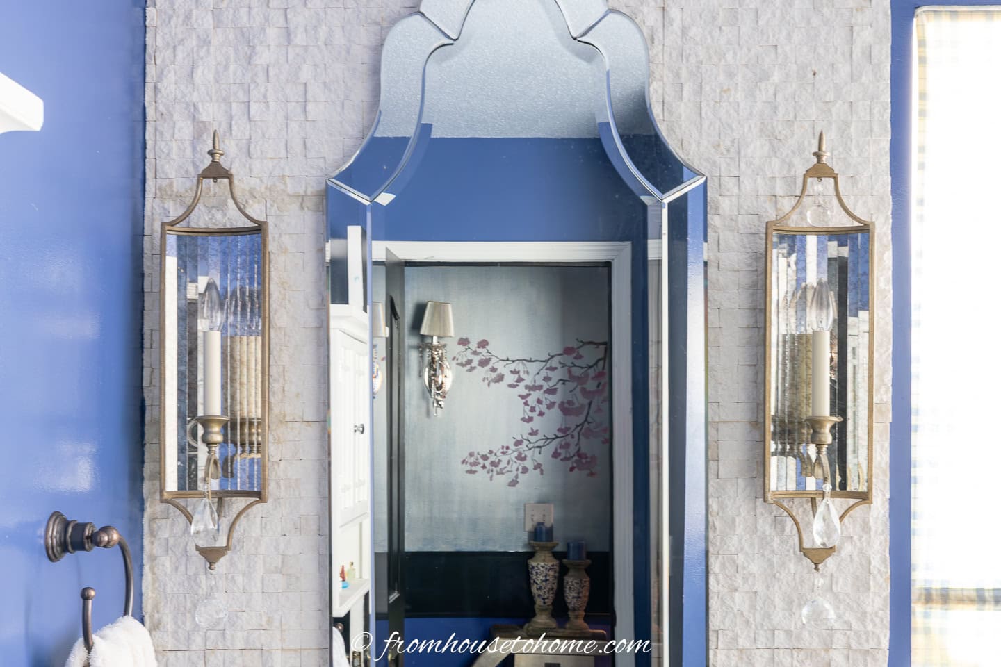 Two gold and mirrored sconces on either side of a tall mirror in a small bathroom