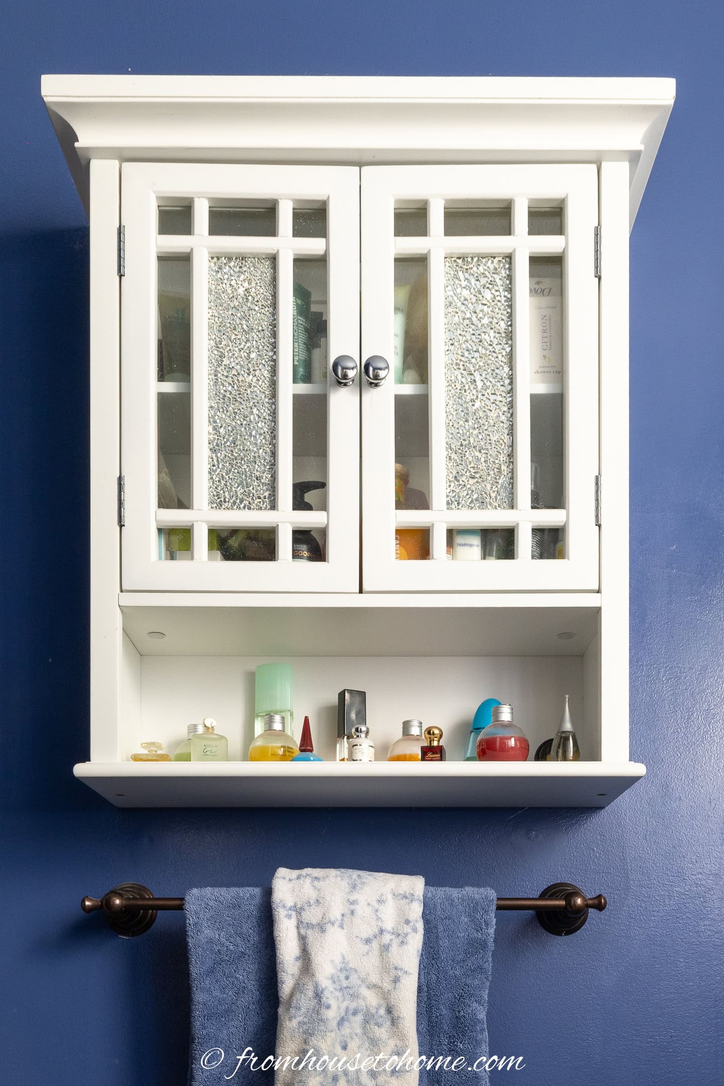 A white bathroom cabinet hung on the wall above a towel rod in a small blue bathroom