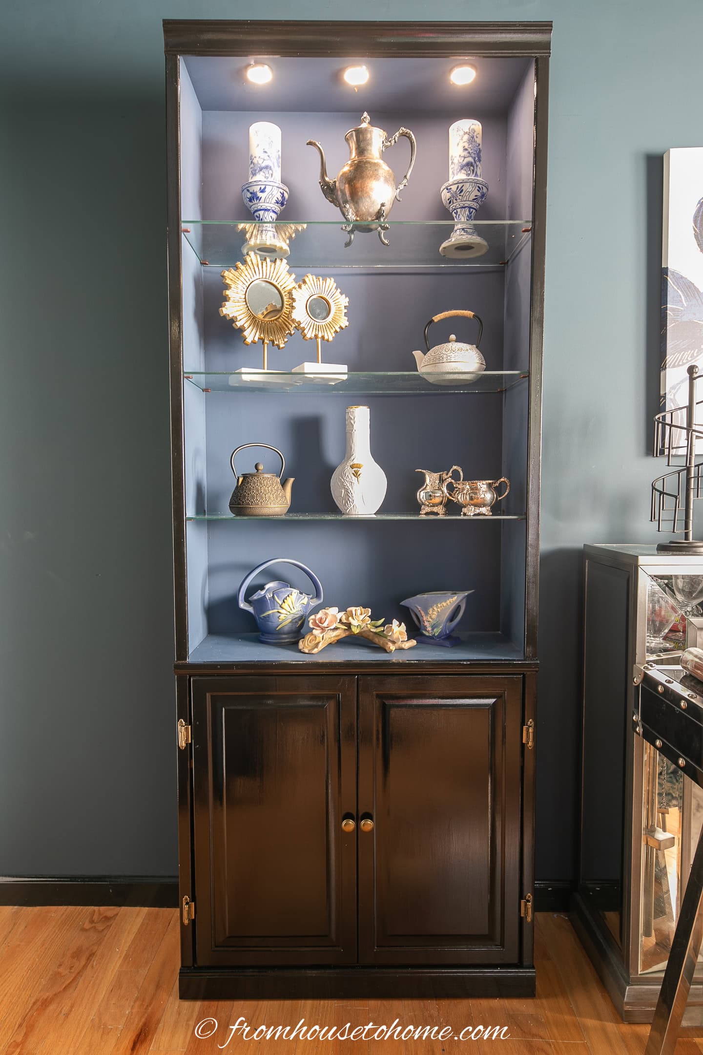 A bookshelf painted with gloss black paint on the outside, blue paint on the inside and glass shelves