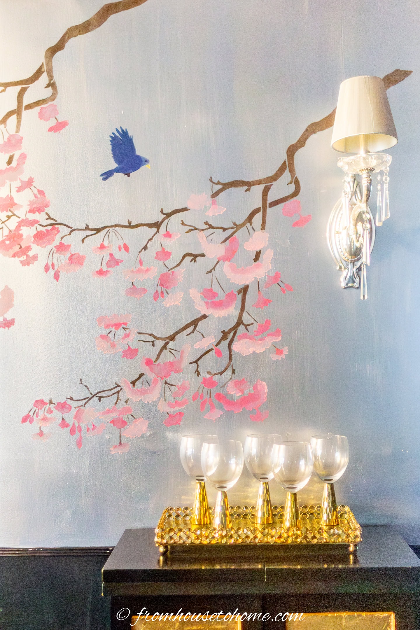 A set of gold-stemmed wine glasses in front of a DIY Chinoiserie wall with pink cherry blossoms