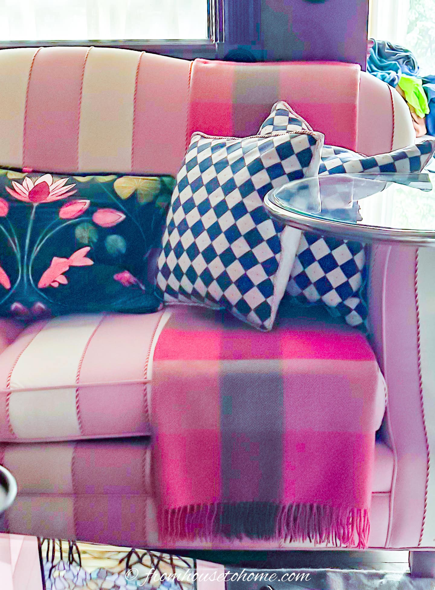 A pink plaid sofa with a pink blanket, two checkered pillows, and a floral cushion sits next to a round metal side table.