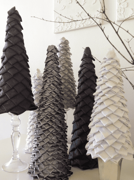 A group of decorative cone-shaped trees in shades of black, gray, and white with a scale-like texture, arranged on a white surface with bare branches in the background.