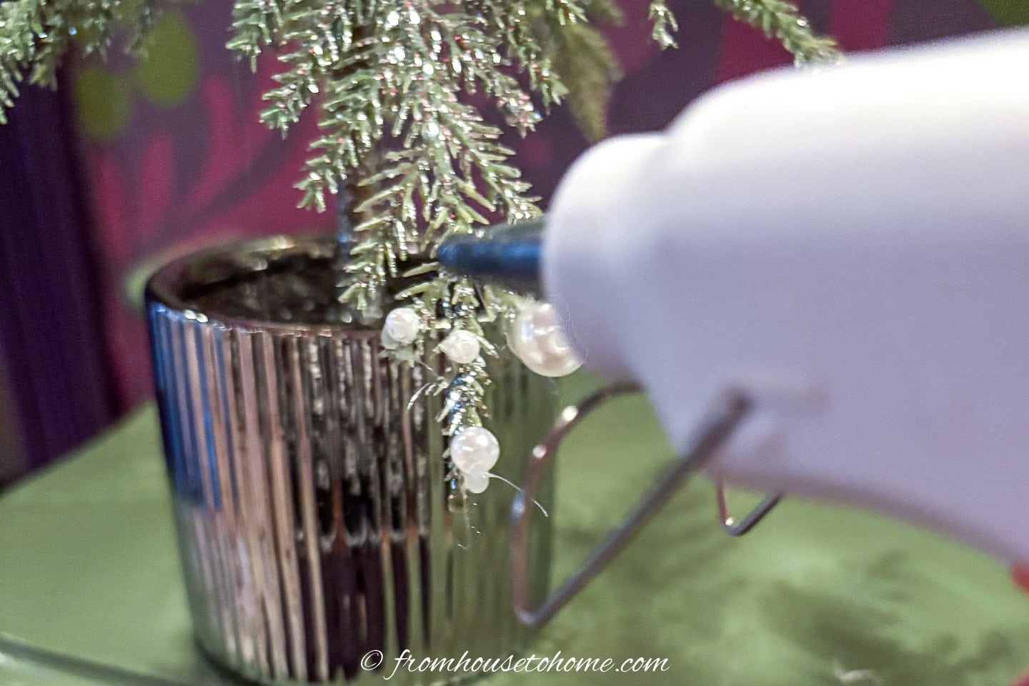 A glue gun putting a ball of glue on a tabletop Christmas tree
