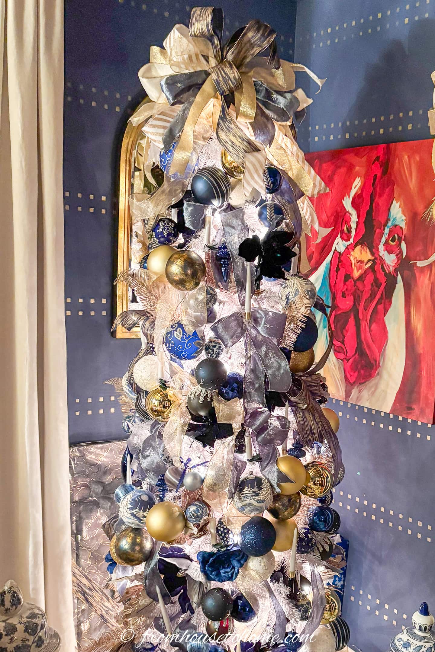 A white Christmas tree decorated with blue, white and gold ribbons and ornaments