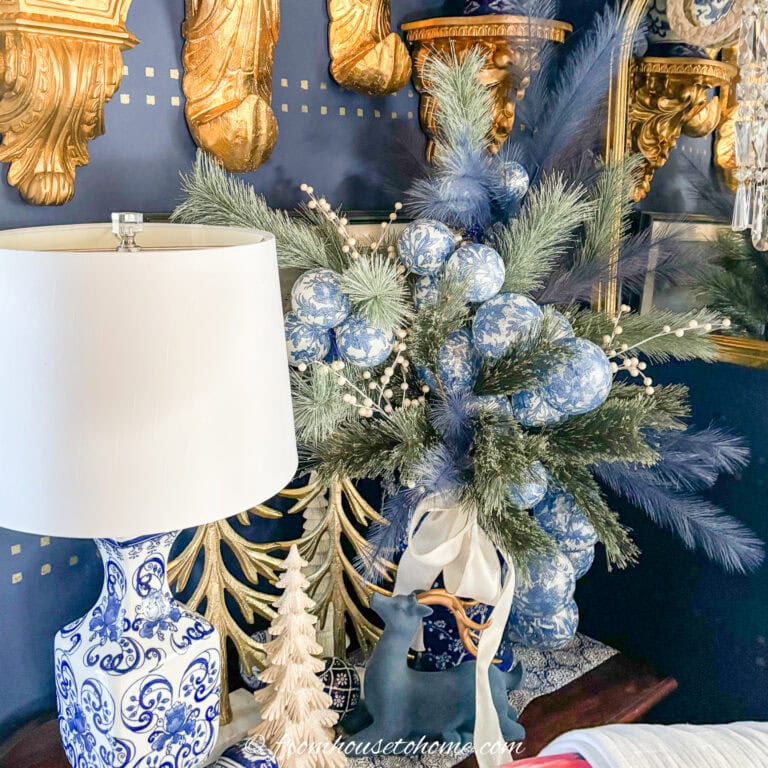 A blue and white Christmas centerpiece made with artificial evergreen boughts, blue and white Chinoiserie ornaments in a ginger jar