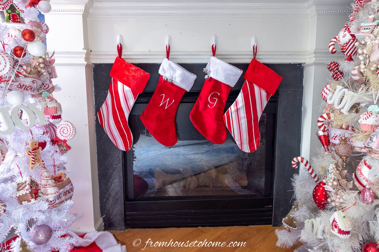 Four red, white and pink stockings hung in front of a fireplace with candyland trees on either side