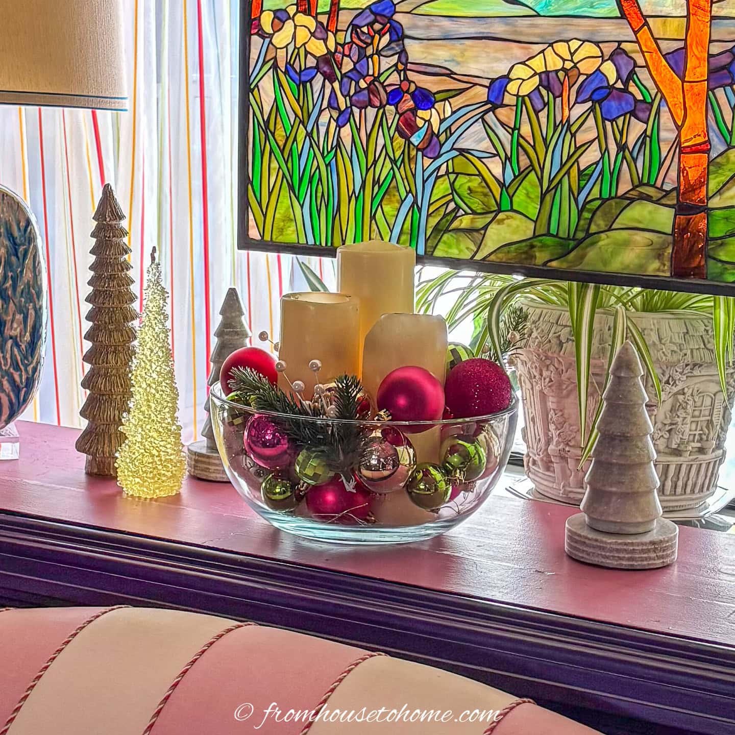 A glass bowl filled with pink and green ornaments and 3 white pillar candles