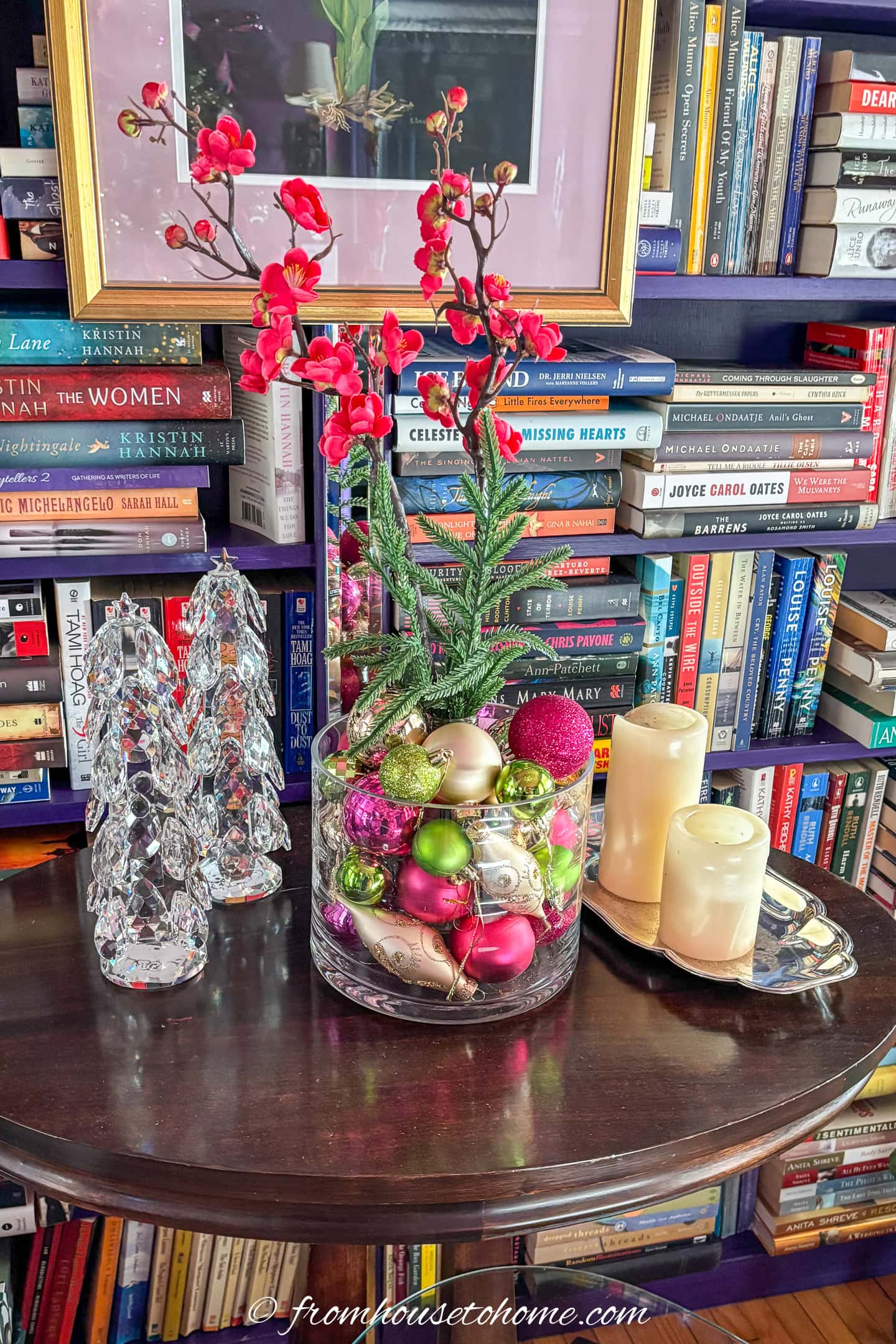 A large glass vase filled with fuchsia, lime green and gold ornmanets with artificial flowers in the middle