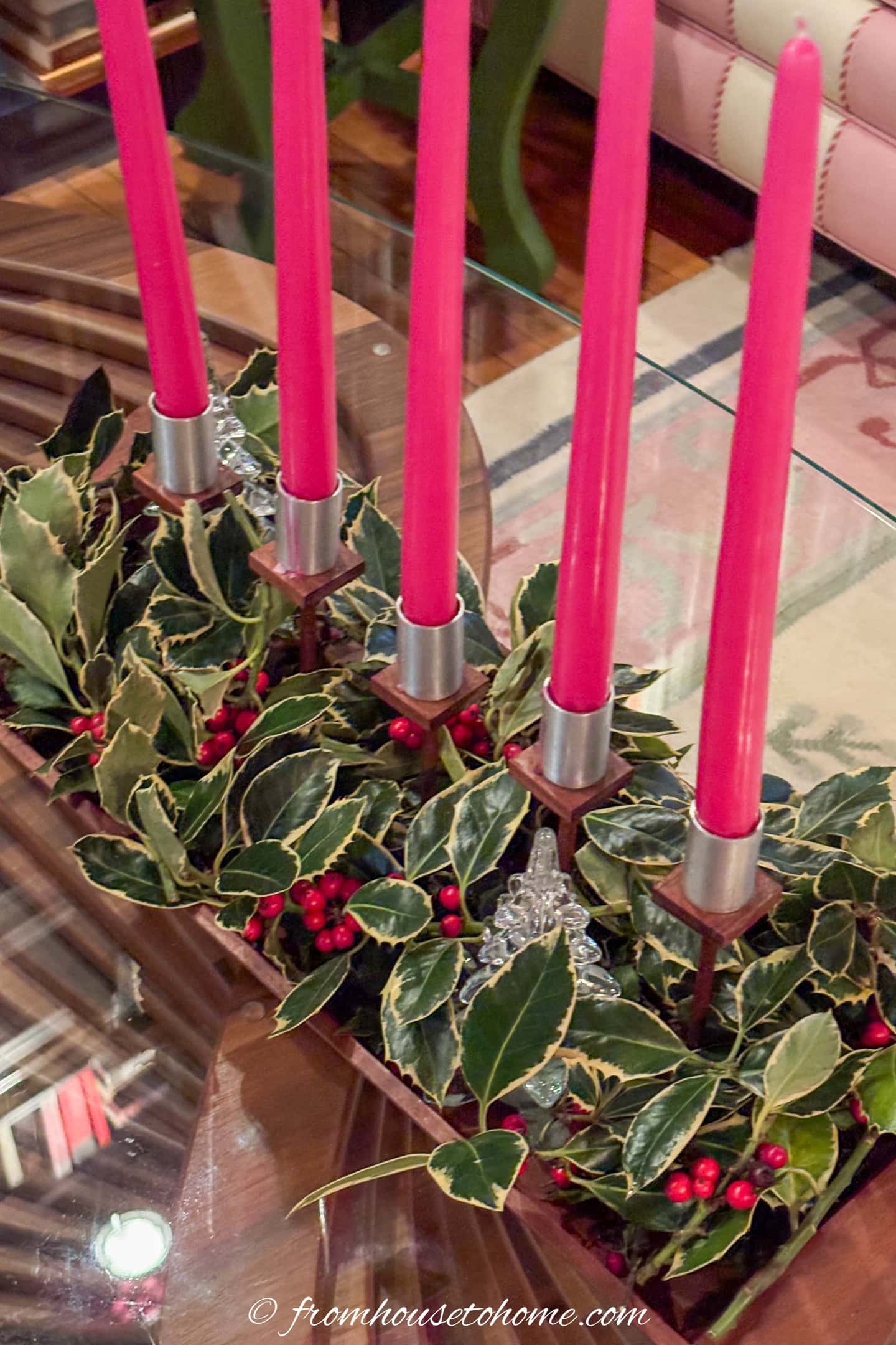 Close up of fuchsia candles in a candlabra with variegated holly at the bottom of them