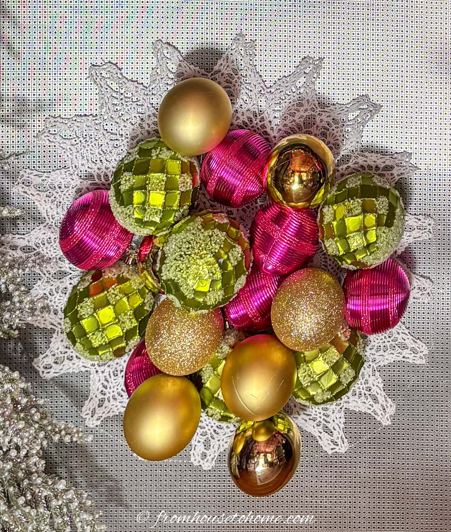 Christmas wall decor made of fuchsia, lime green and gold ball ornaments on a doily background