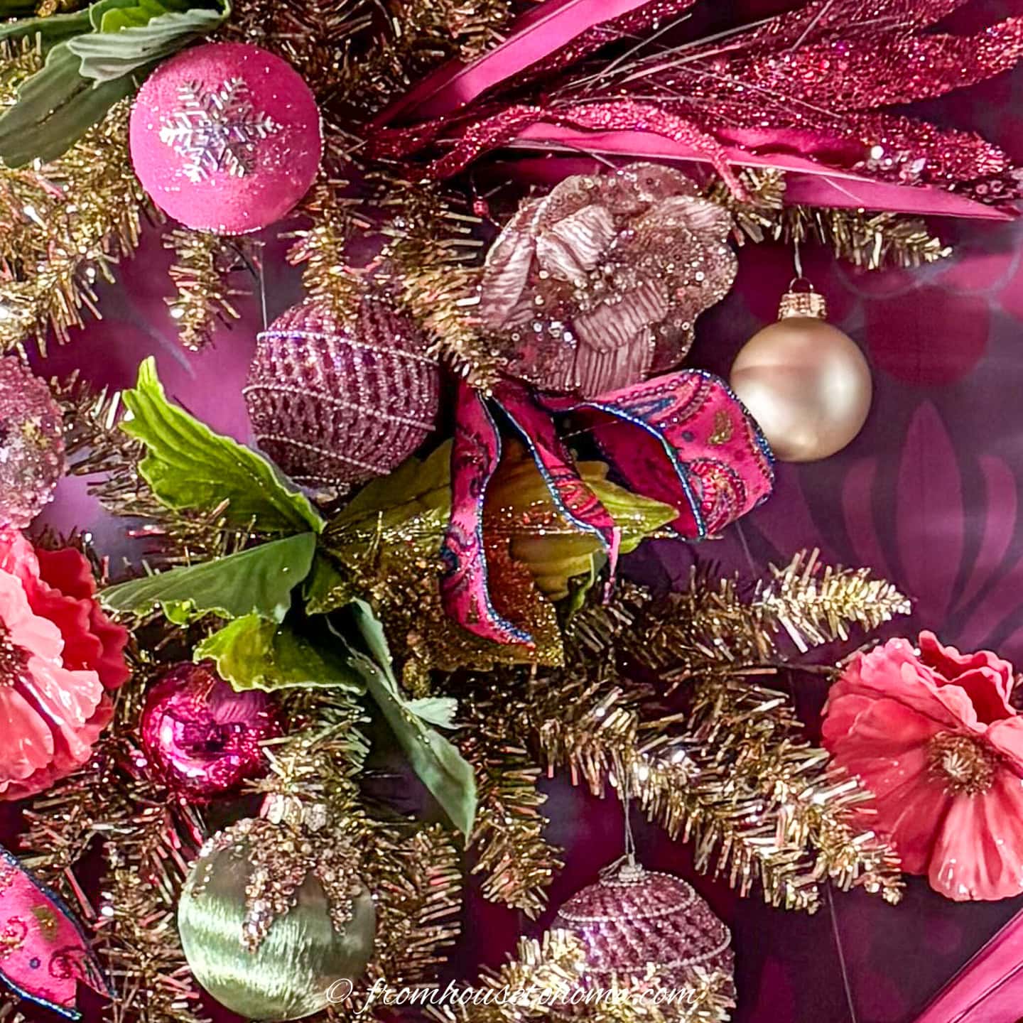 Close up of pink, green and gold ornaments and ribbon on a wall Christmas tree