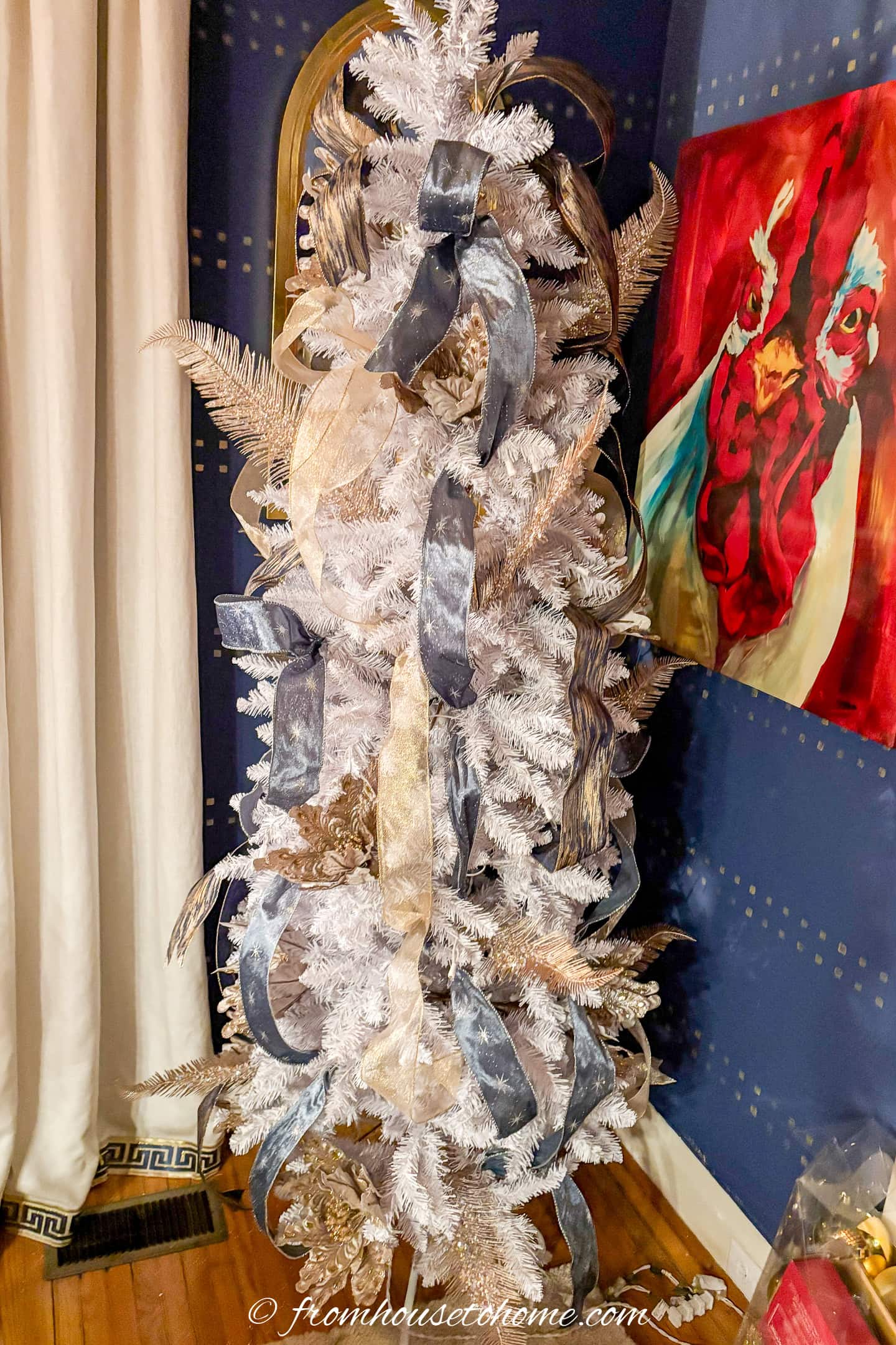 A white Christmas tree with blue and gold ribbons running down the length of it
