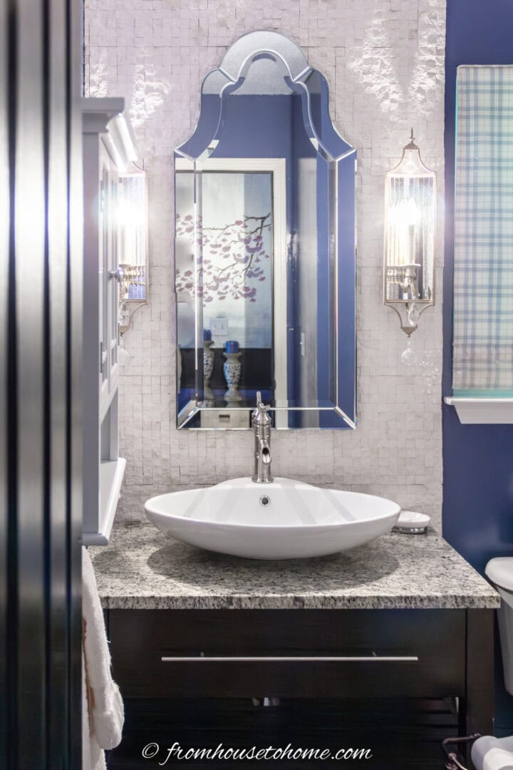 A small bathroom with a large Venetian wall mirror behind the sink that reflects decor from the hallway